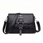 Bolsa clutch feminina transversal preta de couro sintético com aba e argola prateada, vista de frente
