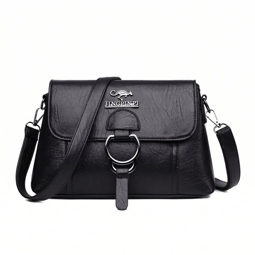 Bolsa clutch feminina transversal preta de couro sintético com aba e argola prateada, vista de frente