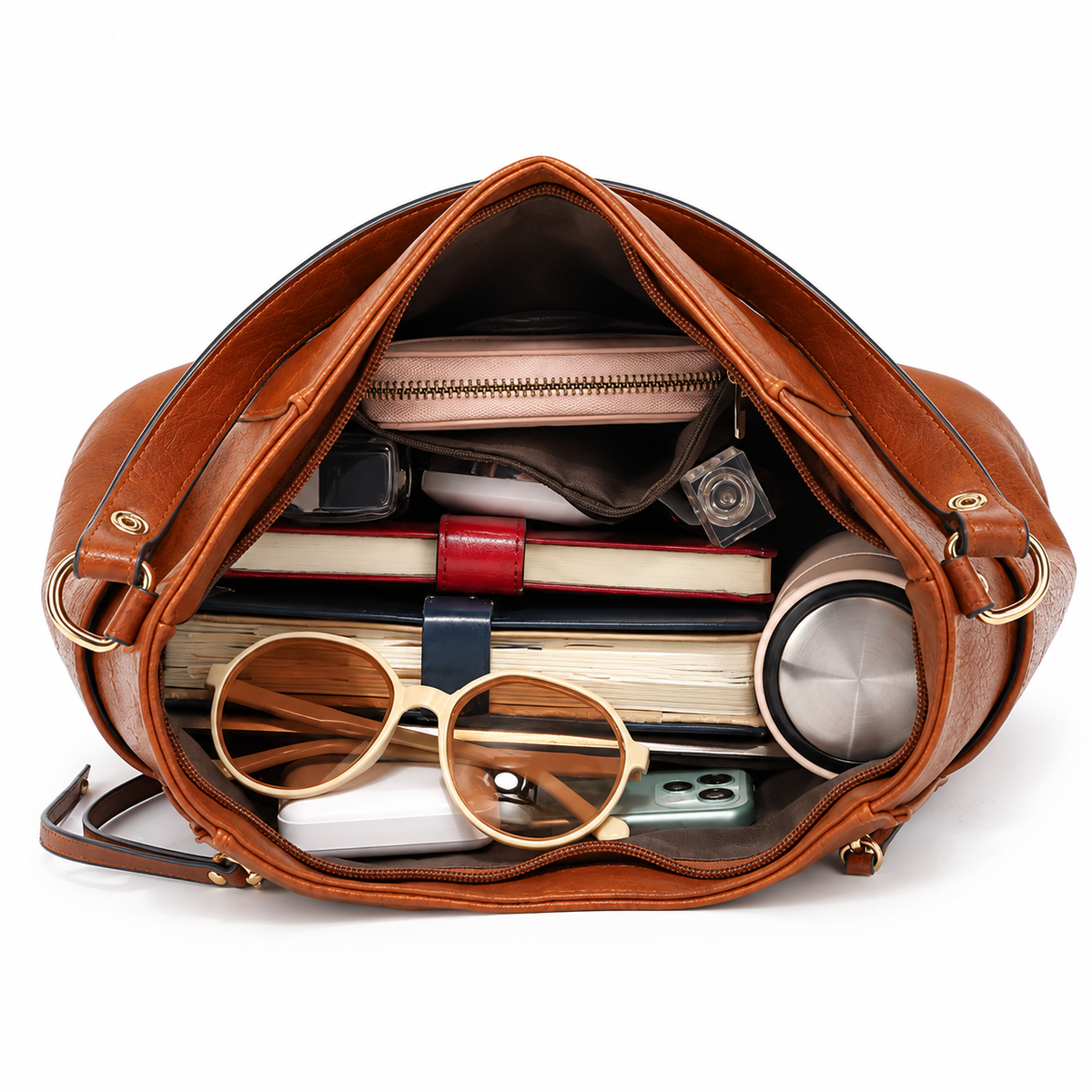 Bolsa tote caramelo aberta e cheia com livro, óculos, carteira e maquiagem